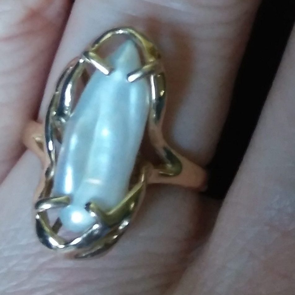 A ring on a finger.  The gem is an irregular pearl.