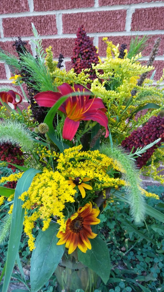 A bouquet of mostly red and/or yellow flowers and green foliage, mostly wild harvested.